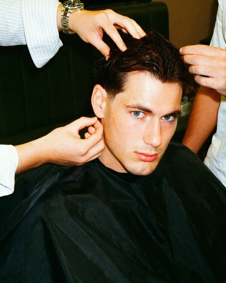 A client in the green salon chair having his hair styled by hand after a cut