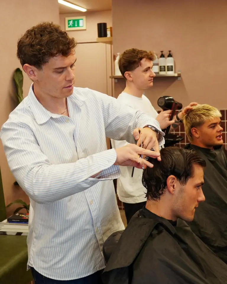 A stylist in a striped shirt cutting a client's hair in the salon